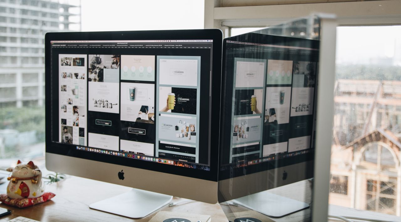 Two monitors on a desk displaying web design in a modern office environment.